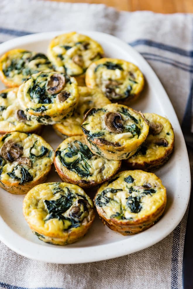 Egg cups with spinach and cheese on an oval platter.