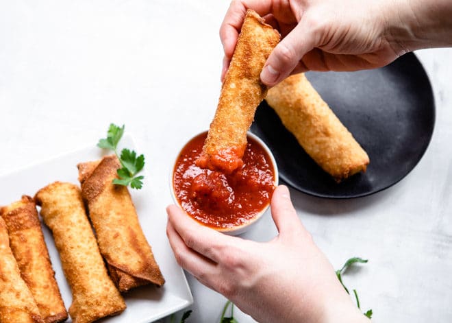 A pizza stick being dipped in marinara sauce.