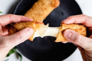 A 3-ingredient pizza stick being pulled open with another stick on a black plate.
