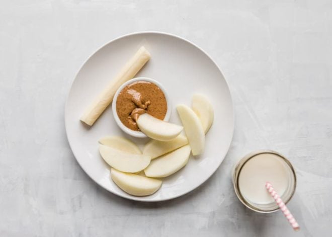 10 Toddler Breakfast Ideas - a photo of multiple apple slices with an apple slice dipping in almond butter and a cheese stick on a white plate and white background - click photo for full written recipes