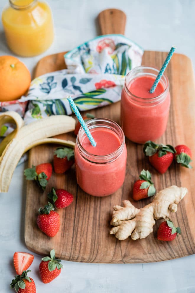 Two strawberry citrus ginger smoothies on a wooden cutting board.