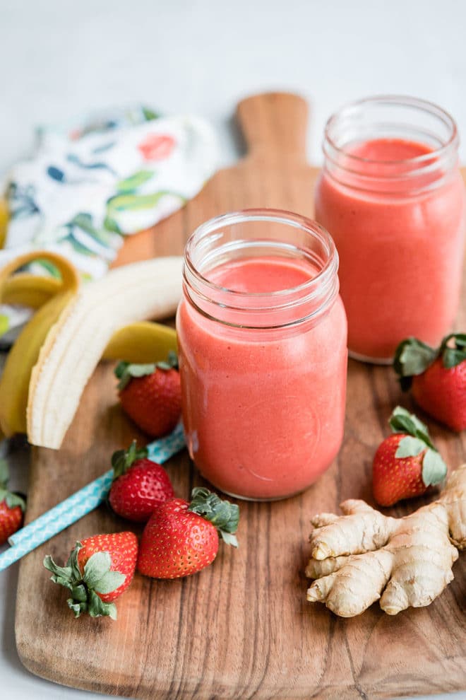 Strawberry and citrus ginger smoothie in glasses on a wooden countertop.