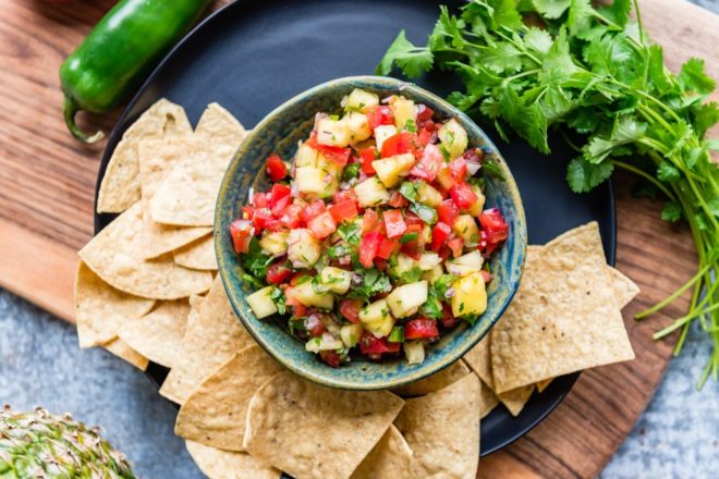 Pineapple salsa in a teal bowl surrounded by tortilla chips.