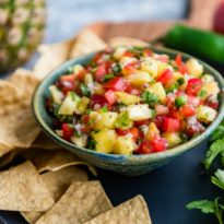 Easy pineapple salsa in a blue bowl surrounded by tortilla chips.