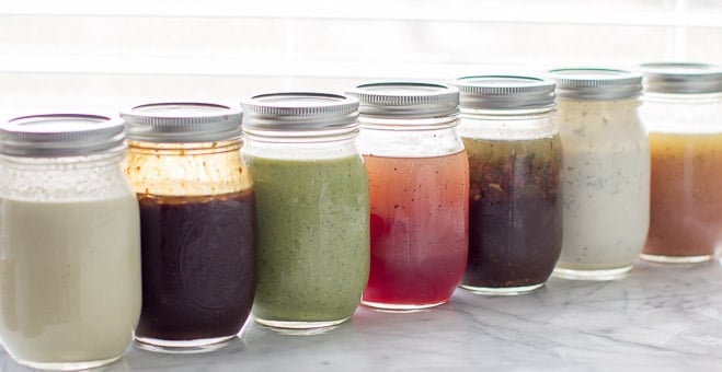 Seven mason jars filled with different salad dressings lined up next to each other. 