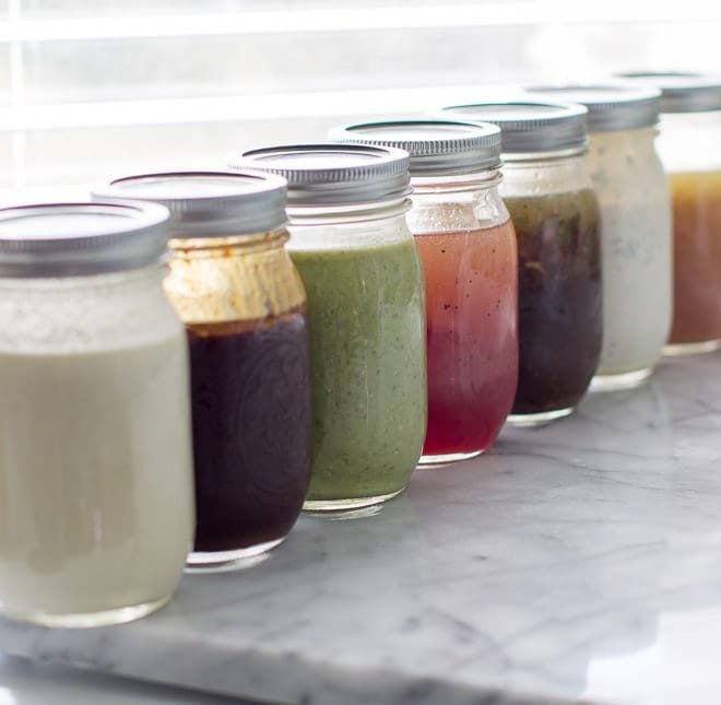 Seven mason jars filled with different salad dressings lined up next to each other. 