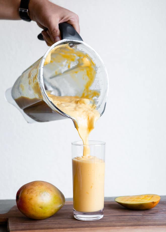 Someone pouring a tropical mango smoothie into a glass.