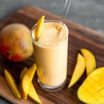 Tropical mango smoothie in a clear glass with a straw and slice of mango as a garnish.