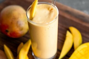 Tropical mango smoothie in a clear glass with a straw and slice of mango as a garnish.