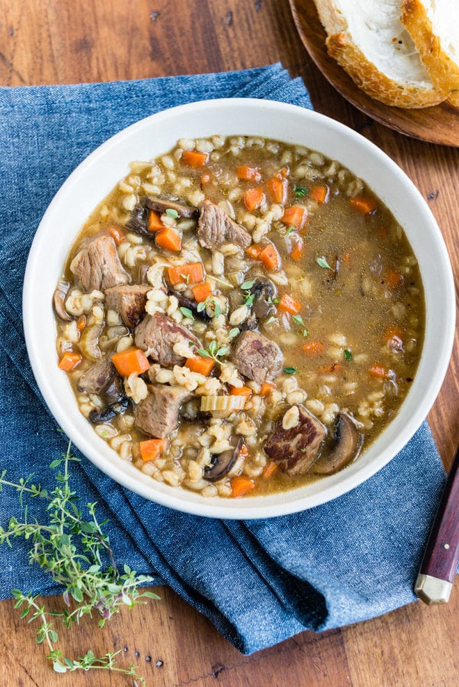 A bowl of slow cooker beef barley soup on a blue linen.
