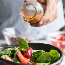 Homemade poppy seed dressing being poured onto a spinach salad.