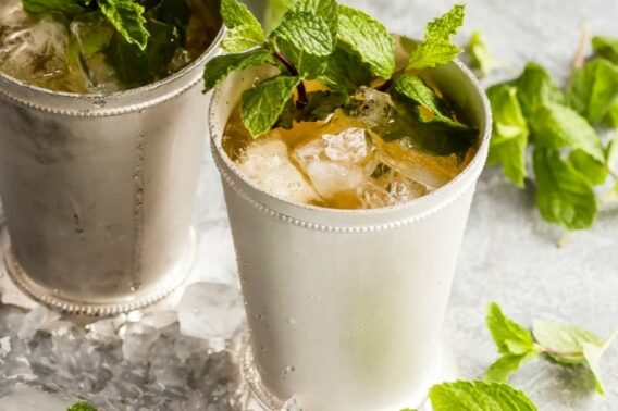Two mint Juleps in silver glasses surrounded by ice and sprigs of mint.