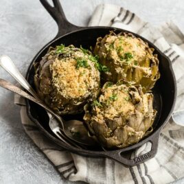 A cast iron skillet with three stuffed artichokes in it.