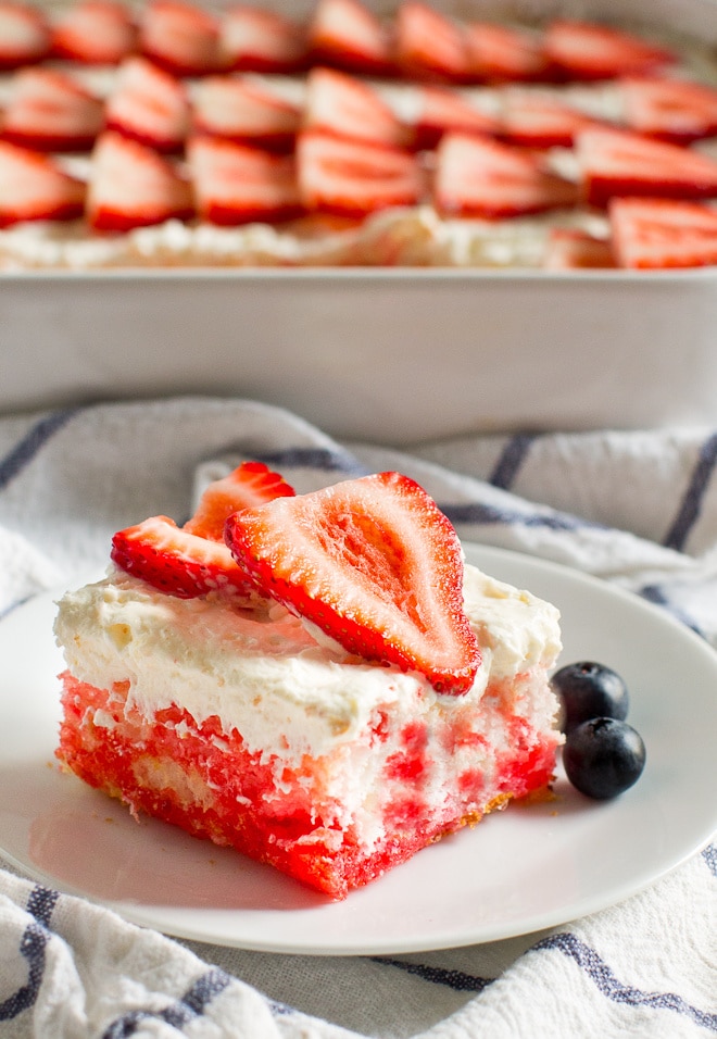 A slice of strawberry jello poke cake topped with strawberries. 