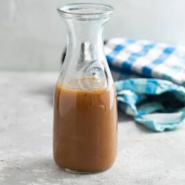 Caramel sauce in a glass bottle on a gray countertop.