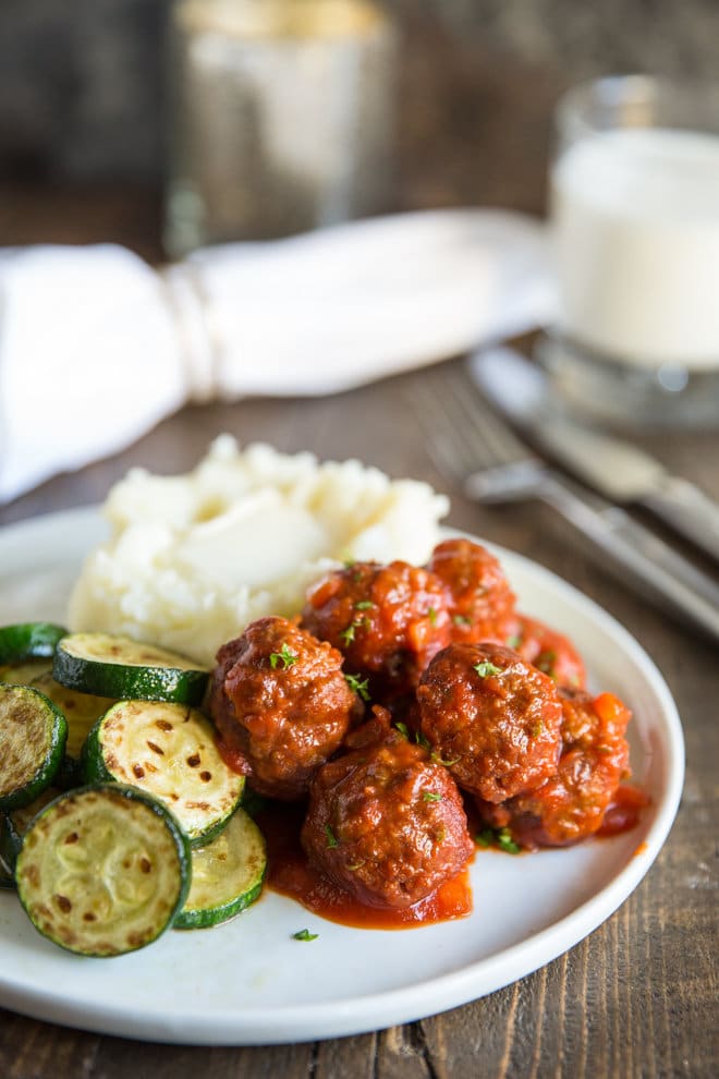 Slow Cooker Meatloaf Meatballs on a white plate with a side of mashed potatoes and roasted sliced cucumbers.