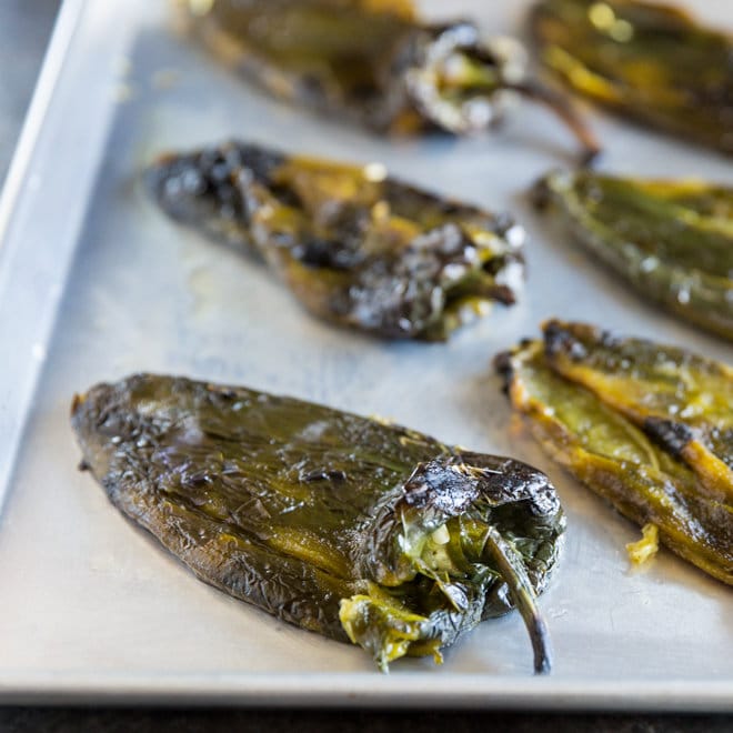 Roasted poblano chiles that have been skinned and seeded on a sheet pan.