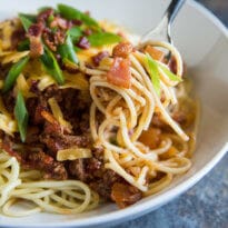 A white bowl of Cowboy Spaghetti with a fork with swirled spaghetti.