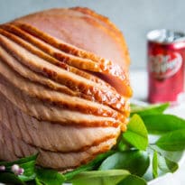 Dr. Pepper Ham spirally cut on a white serving platter with sprigs of green leaves.