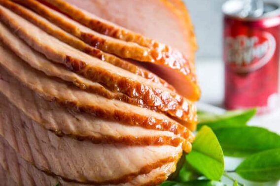 Dr. Pepper Ham spirally cut on a white serving platter with sprigs of green leaves.