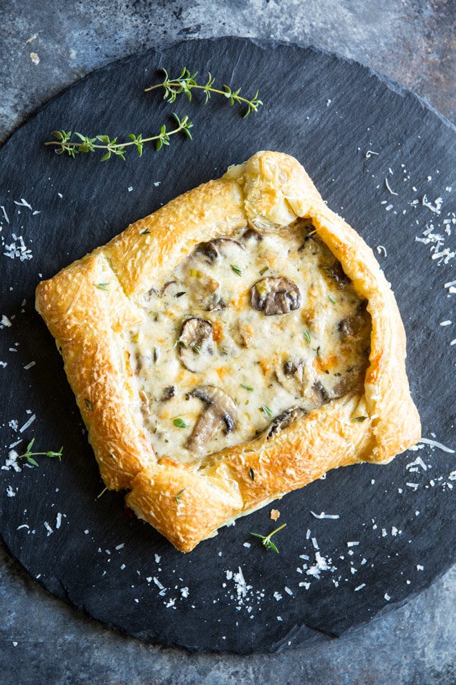 A mushroom and leek tart topped with Freshly green thyme and freshly grated Parmesan cheese on a black plate. 