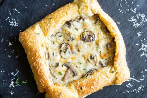 A mushroom and leek tart topped with Freshly green thyme and freshly grated Parmesan cheese on a black plate.
