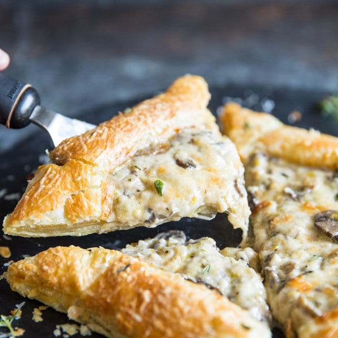 A mushroom and leek tart cut into four pieces with one being lifted out. 