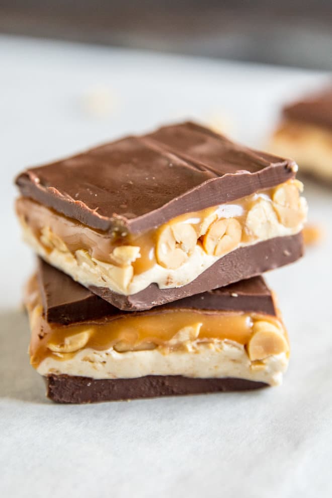 Two homemade snickers bars stacked on top of each other on parchment paper. 