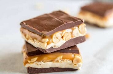 Two homemade snickers bars stacked on top of each other on parchment paper.