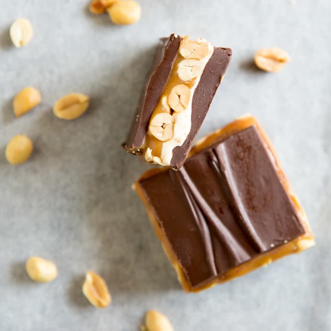 Two homemade snickers bars on parchment paper surrounded by peanuts. 