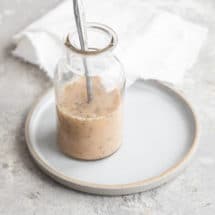 The best homemade Italian dressing in a clear jar with a spoon on a white plate.