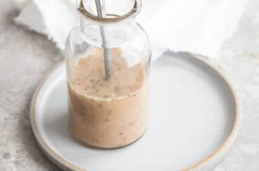 The best homemade Italian dressing in a clear jar with a spoon on a white plate.