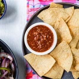 Copycat chipotle hot salsa in a white dish on a black plate with tortilla chips.