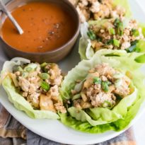 Chicken lettuce wraps on a white plate with a side of sauce.