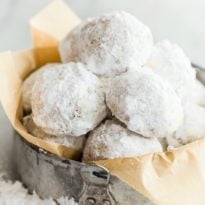Mexican wedding cookies in a sliver tin on parchment paper.