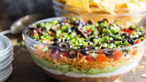 This 7 Layer Dip recipe is made with beans, sour cream, guacamole, cheese, tomatoes, olives, and scallions. It's easy to make and always a hit at parties!