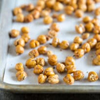 A side shot of roasted chickpeas on a baking sheet with parchment paper.