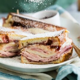 A monte cristo sandwich on a white platter being dusted with powdered sugar.