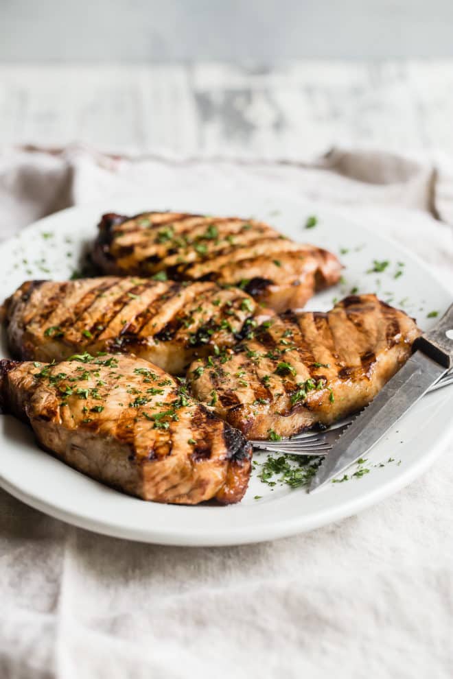 Four grilled pork chops on a white plate.