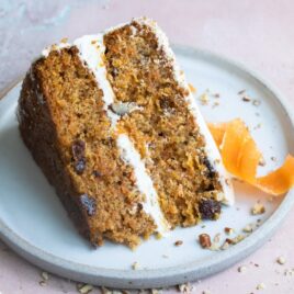 A slice of carrot cake on a blue plate with a candied carrot peel.