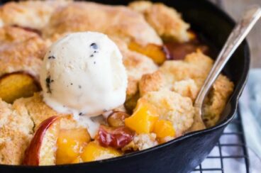 Peach cobbler in a black cast iron with a scoop of ice cream.