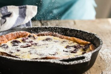 Cherry clafoutis in a black cast iron skillet being sprinkled with powdered sugar.