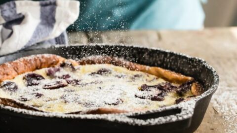 Cherry clafoutis in a black cast iron skillet being sprinkled with powdered sugar.