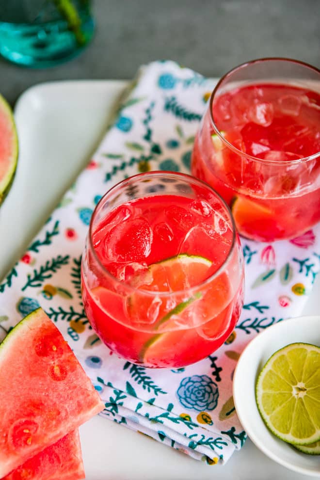Two glasses of agua fresca on a serving platter next to a slice of watermelon.