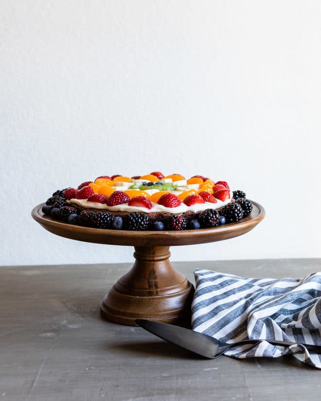 A brownie pizza on a raised wooden cake stand.