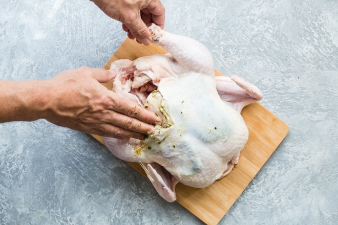 A chicken being rubbed with pesto.