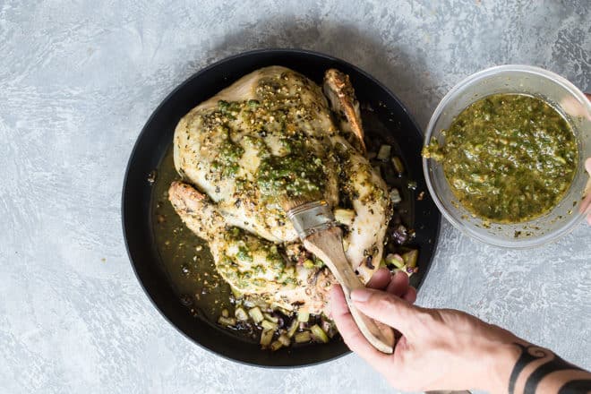 Someone brushing additional pesto over a pesto roasted chicken after being baked.