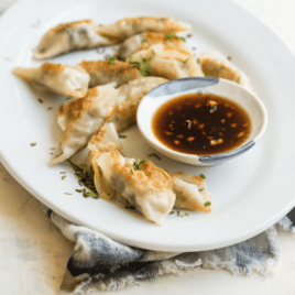 Potstickers on a white plate with a side of dipping sauce.