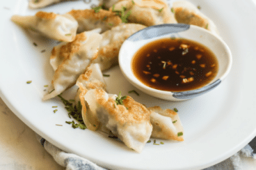 Potstickers on a white plate with a side of dipping sauce.