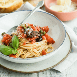 Spaghetti alla Puttanesca in a white bowl with a silver fork.